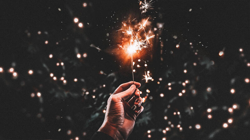 A hand holding a lit sparkler on a black background making a visual allusion to the shape of the Diagram logo