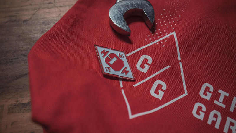 Logo with enamel pin and wrench laying on a red canvas tote bag